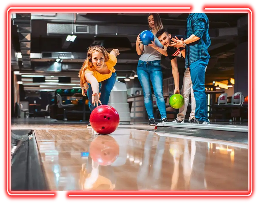 Woman releasing a red bowling ball down the lane while friends watch at Victory Lanes in Decatur, IL